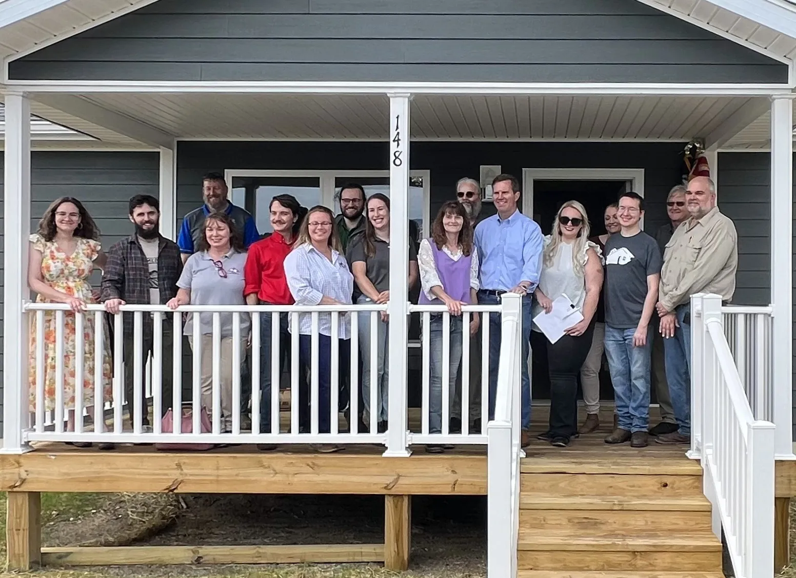 People involved in providing the Neace family a new home pose on its porch in Perry County’s Blue Sky subdivision. Melissa Neace stands between the central porch pole and Gov. Andy Beshear